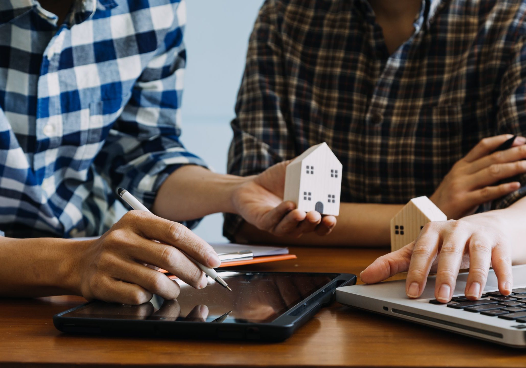 Two people reviewing architectural house plans on a wooden table.