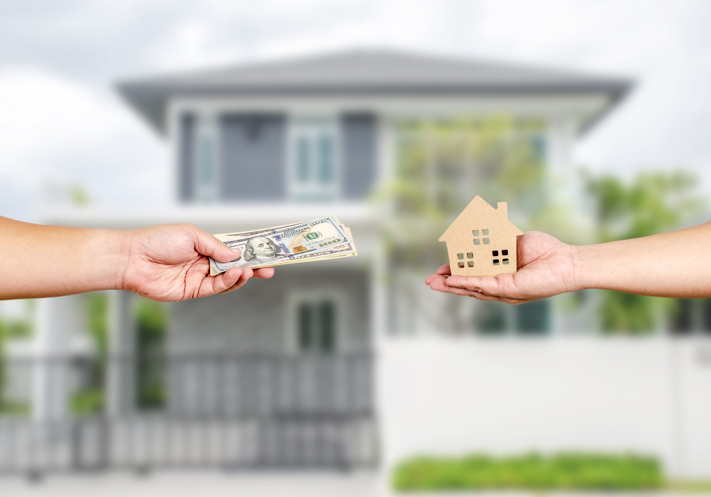 Hands exchanging a stack of money for a small house model.