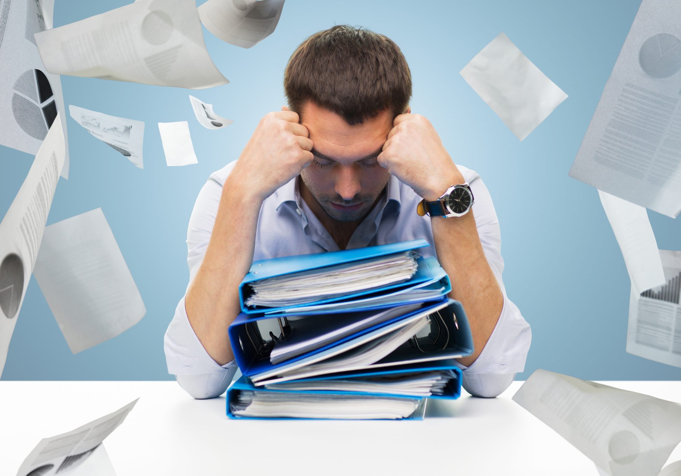 Man at a desk looking overwhelmed by a mountain of paperwork and house documents.