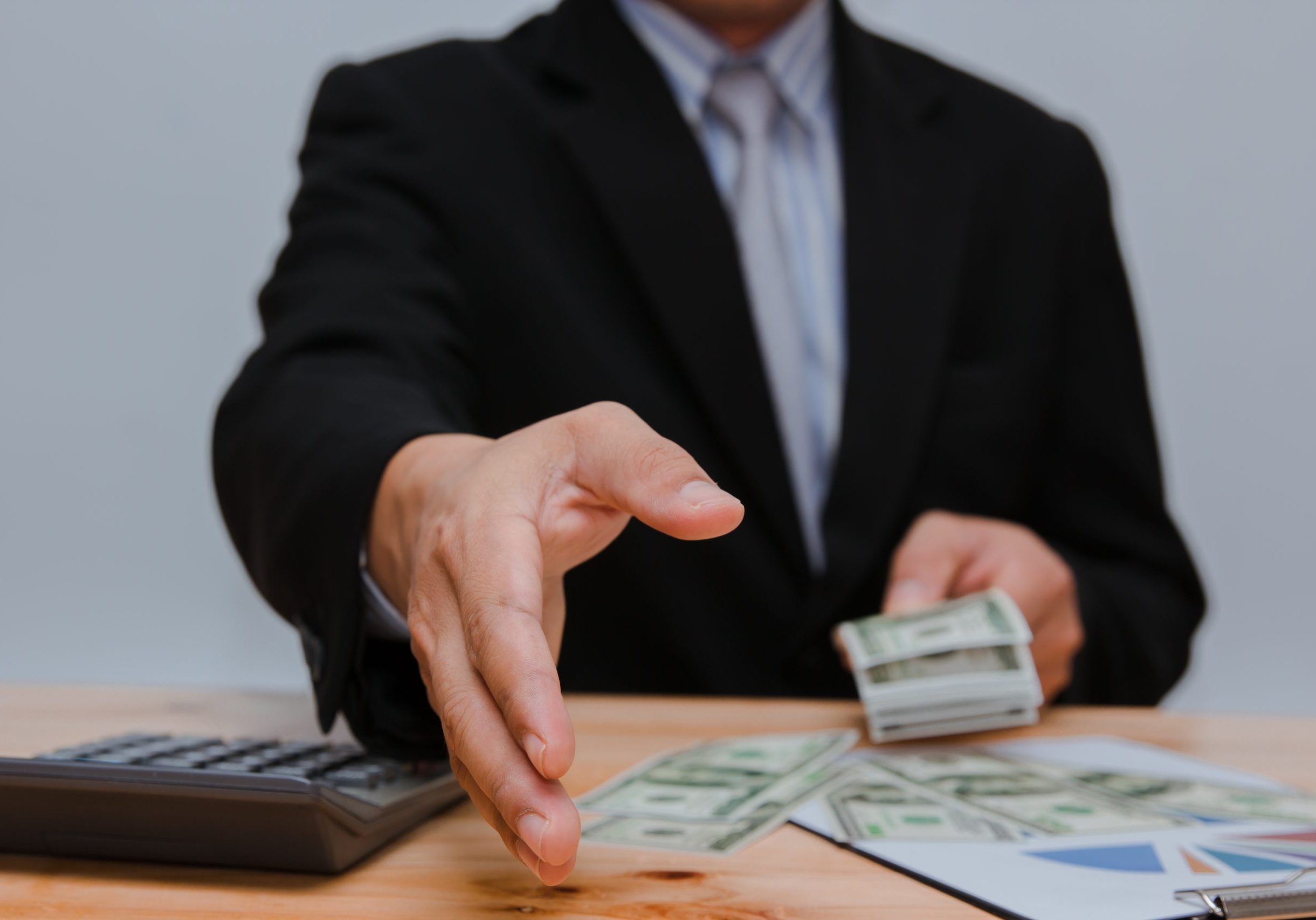 Close-up of a professional in a suit handing over a stack of cash.