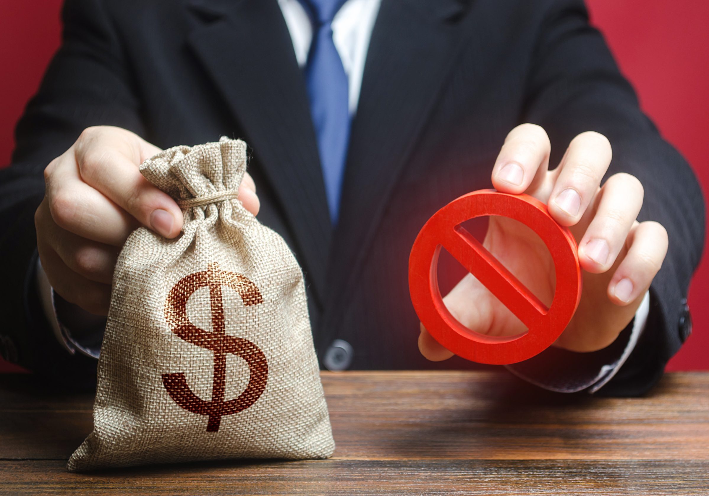 Professional holding a bag of cash next to a red "No" symbol.