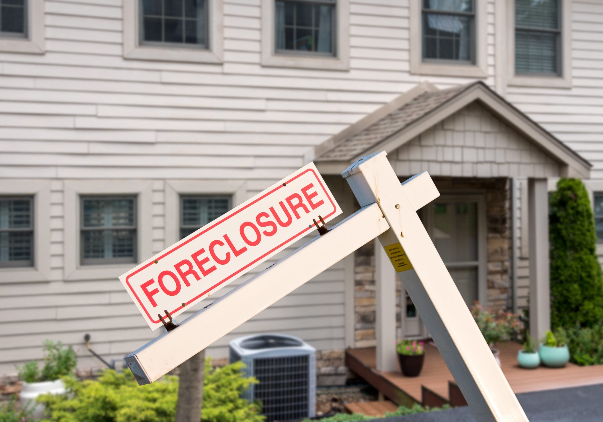 Close-up of a wooden "FORECLOSURE" sign in the front yard of a suburban house.