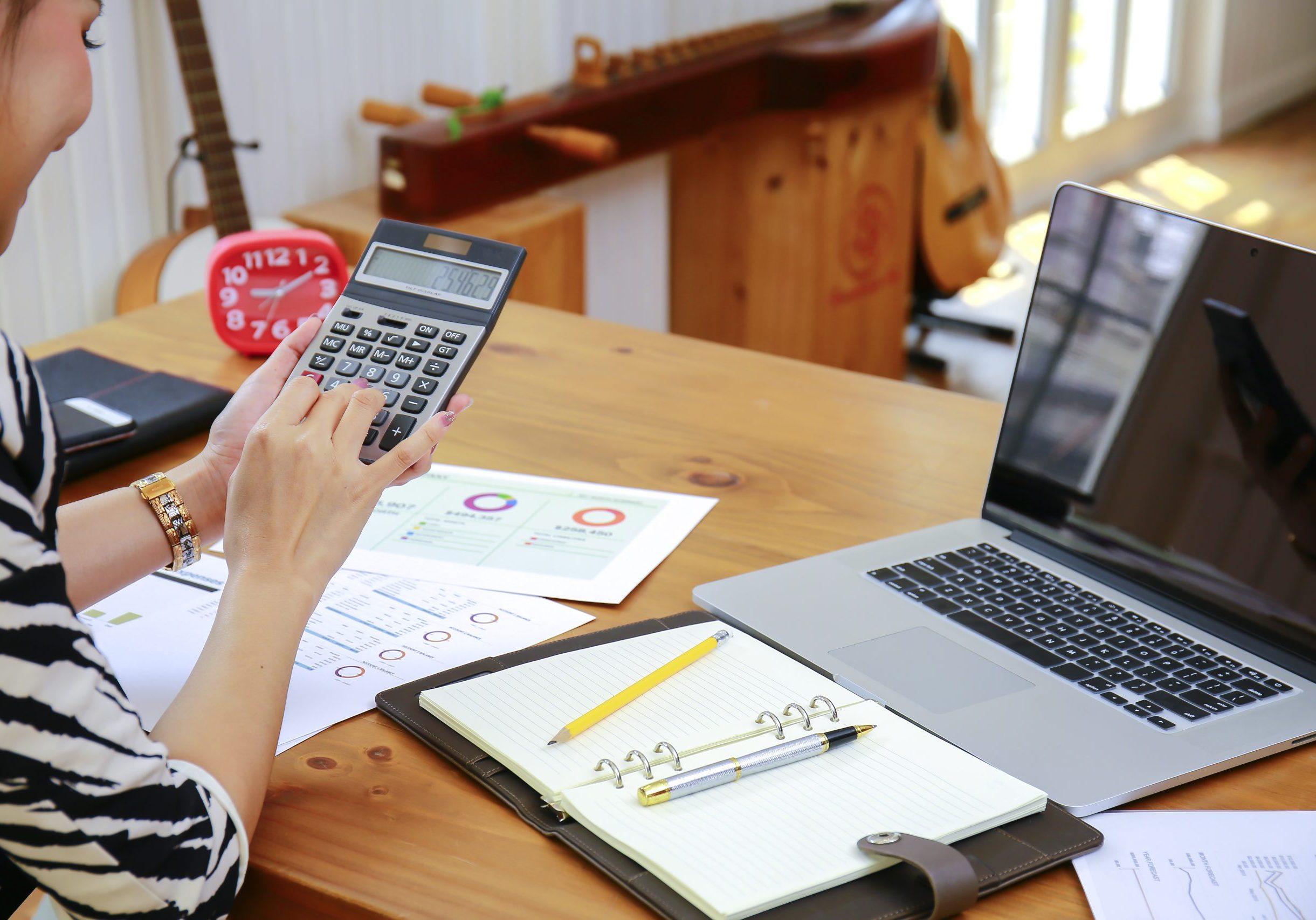 Person using a calculator at a desk with a laptop and architectural blueprints.